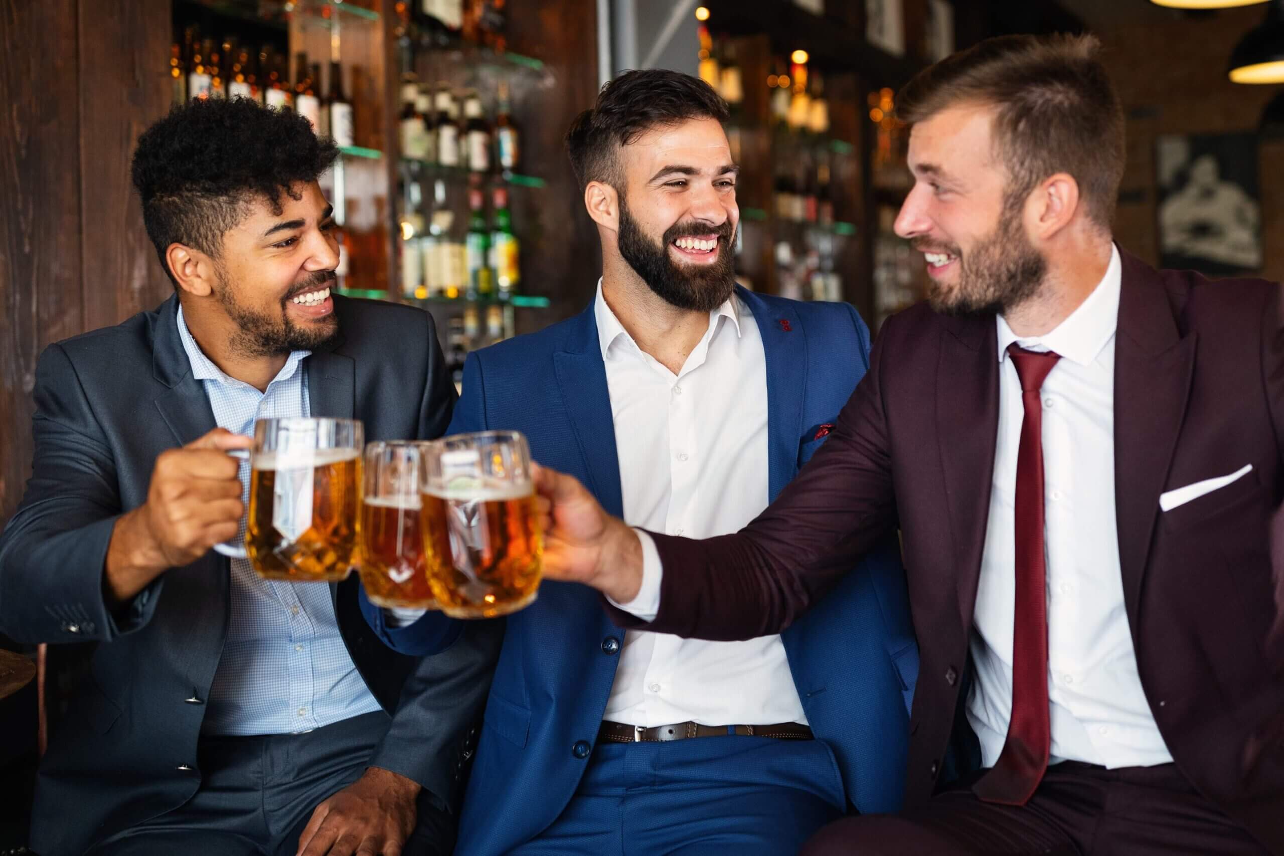 Happy handsome young businessmen drinking beer and talking at pub after work